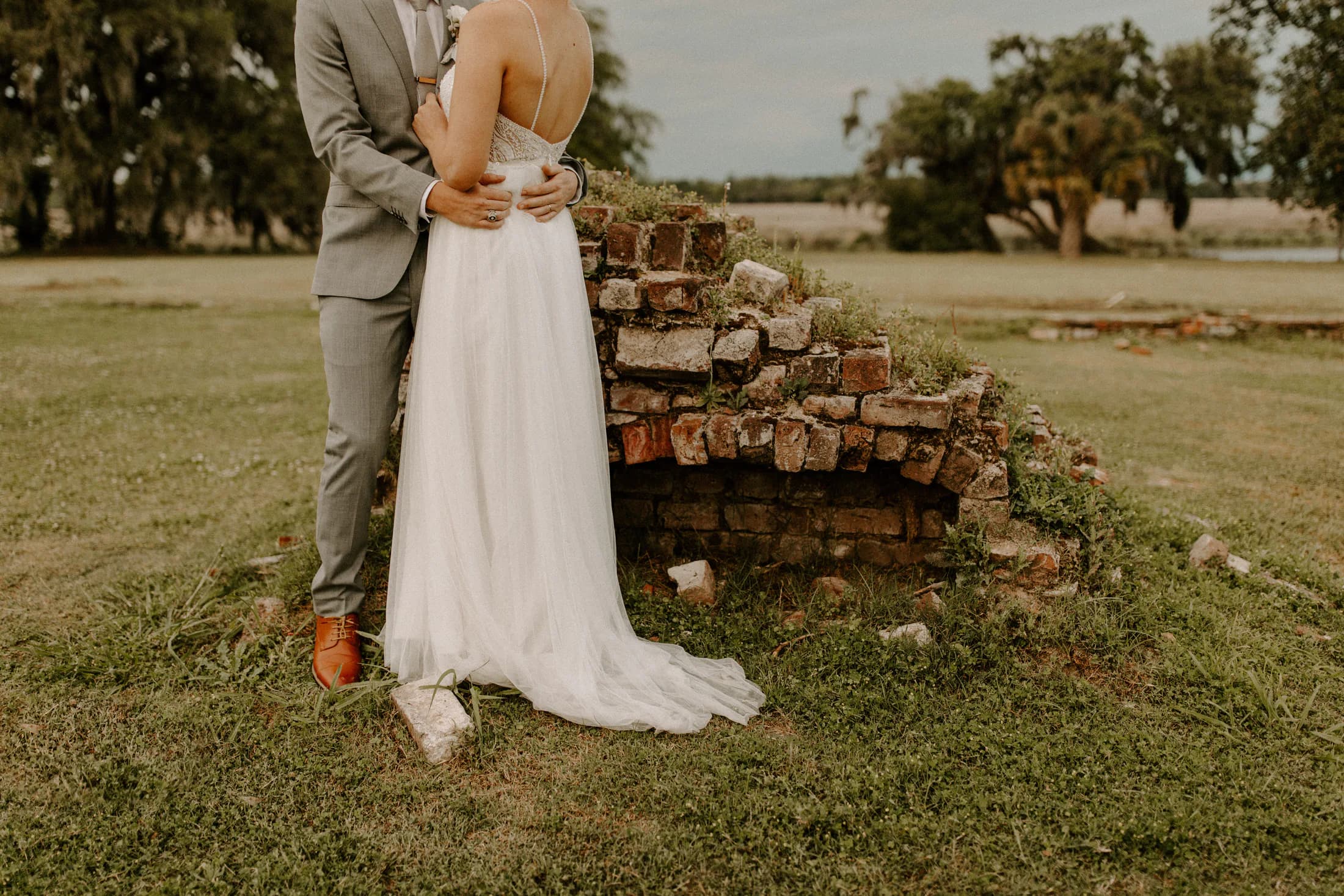Emma and Joel standing beside an old brick structure on their wedding day